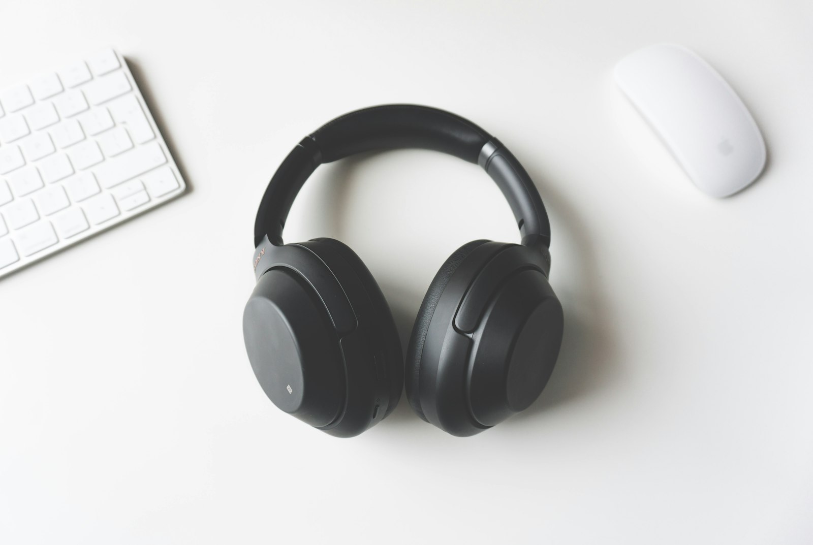 Wireless headphones resting on a desk between a keyboard and a mouse