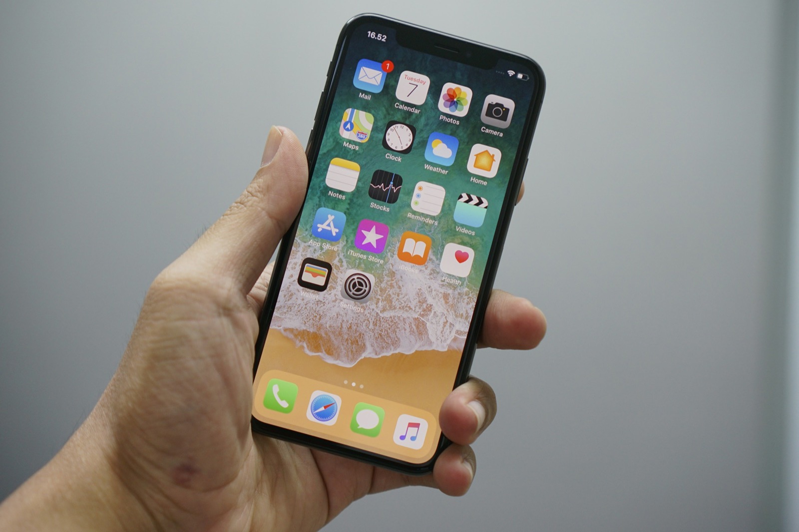 A hand holding an iPhone with its home screen of app icons lit up against a plain grey background