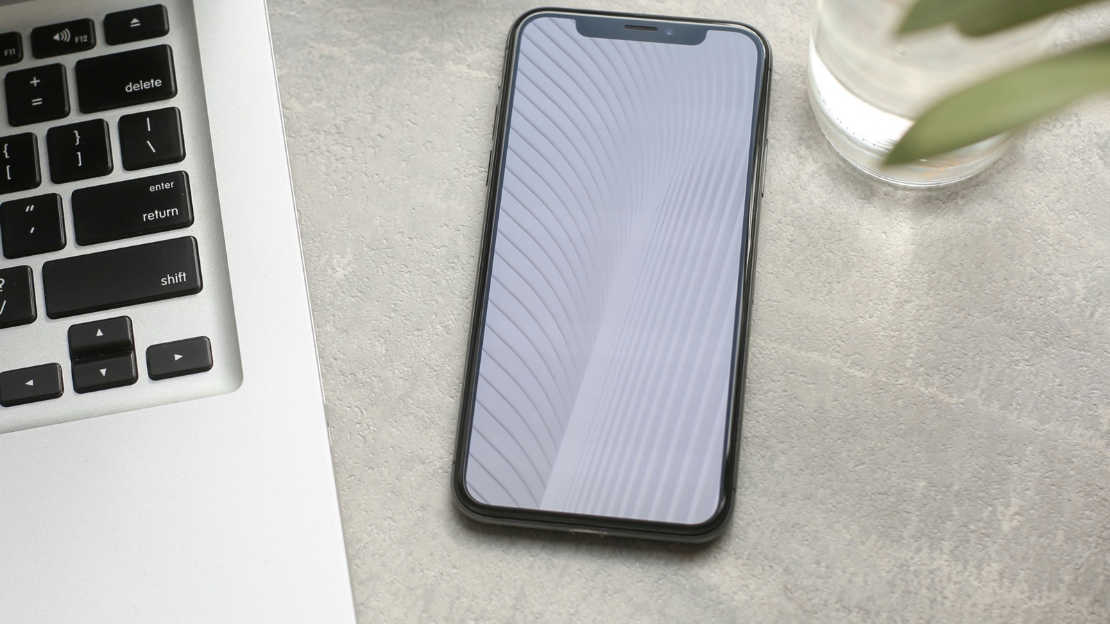 A black smartphone lying on top of a MacBook Pro keyboard, shot from directly above in a workspace flatlay