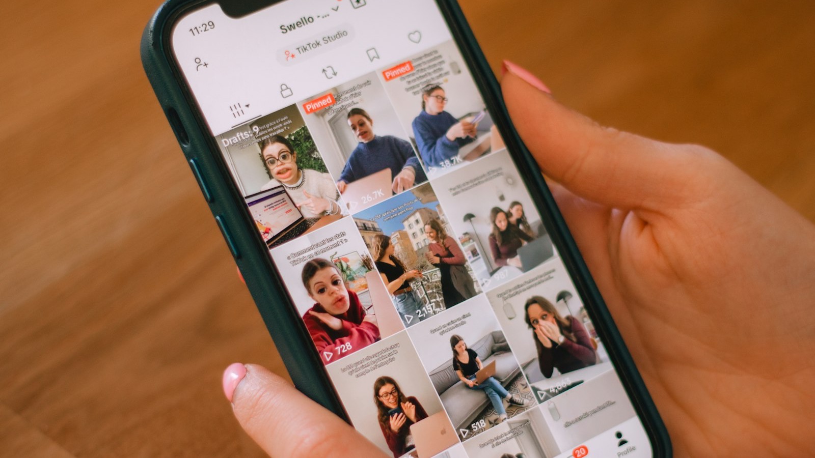 A hand holding a phone mid-scroll through a short-form video feed, thumb paused over the screen