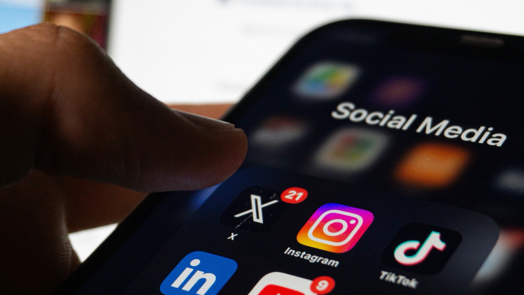 A hand holding a phone showing a home screen with Instagram, TikTok, X, and LinkedIn app icons