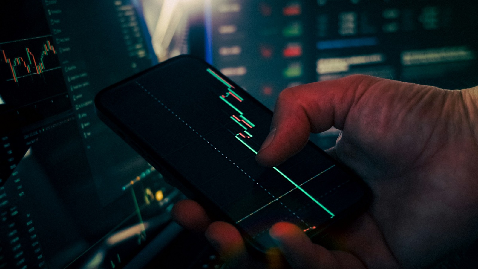 Close-up of a hand holding a phone showing candlestick stock chart data on screen